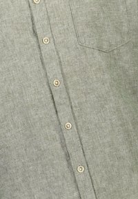 Camicia di lino verde chiaro con bottoni frontali, dotata di taschino sul petto e bottoni dello stesso colore del tessuto. Materiale testurizzato e traspirante.