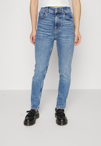 Ljusblå högmidjade skinny jeans med subtil blekning, fem fickor och kontrasterande sömmar. Matchas med svarta snörskor.