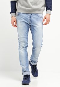 Ljust blå denimjeans med slim fit, lätt blekning och uppvikt fåll. Kombinerat med mörkblå sneakers och en grå sweatshirt.