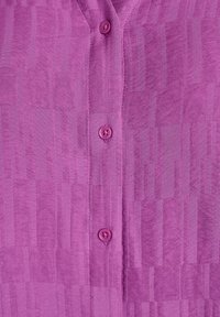 Fialová košeľa so zapínaním na gombíky, vyrobená z textúrovanej látky s vertikálnymi pruhmi a zodpovedajúcimi gombíkmi vpredu.