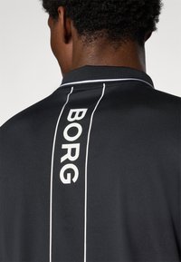 Svart polo skjorte med en hvit vertikal stripe og teksten "BORG." Designet med en teksturert finish og en tradisjonell krage.