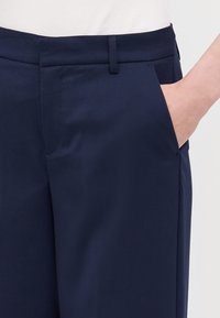 Marineblauwe, op maat gemaakte broek met een zachte textuur, zijzakken en een rechte tailleband. Geen zichtbare sluitingen of versieringen.