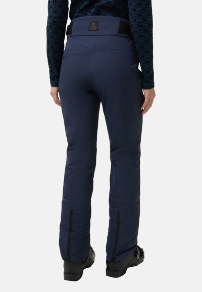 Granatowe spodnie narciarskie z gładkiego, izolowanego materiału; mają zamki błyskawiczne przy kostkach oraz regulowany pas. Widok z tyłu pokazuje detale szwów.