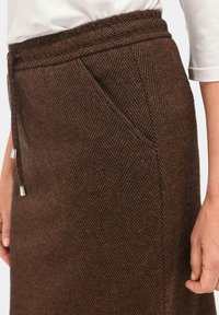 Jupe marron en chevrons faite de tissu texturé, dotée d'une taille à cordon avec des accents métalliques et de poches latérales pour plus de fonctionnalité.