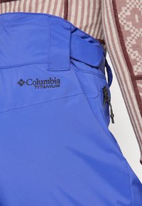 Blauwe Columbia Titanium broek met een verstelbare tailleband, zijzak met rits en een gladde textuur. Kenmerkt een logo dat op de voorkant is gestikt.