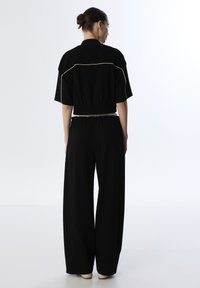 Schwarze, cropped Jacke mit elastischem Saum, verziert mit weißen Abschlüssen. Kombiniert mit schwarzen weiten Hosen. Glattes Material, minimalistisches Design.