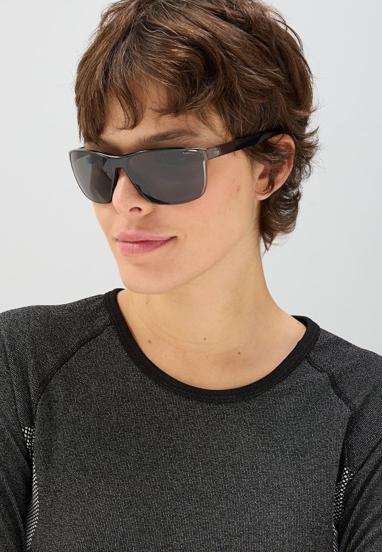 Okulary przeciwsłoneczne z elegancką czarną oprawą i ciemnymi soczewkami. Projekt charakteryzuje się subtelnymi akcentami i kształtem otaczającym, co nadaje nowoczesny wygląd.