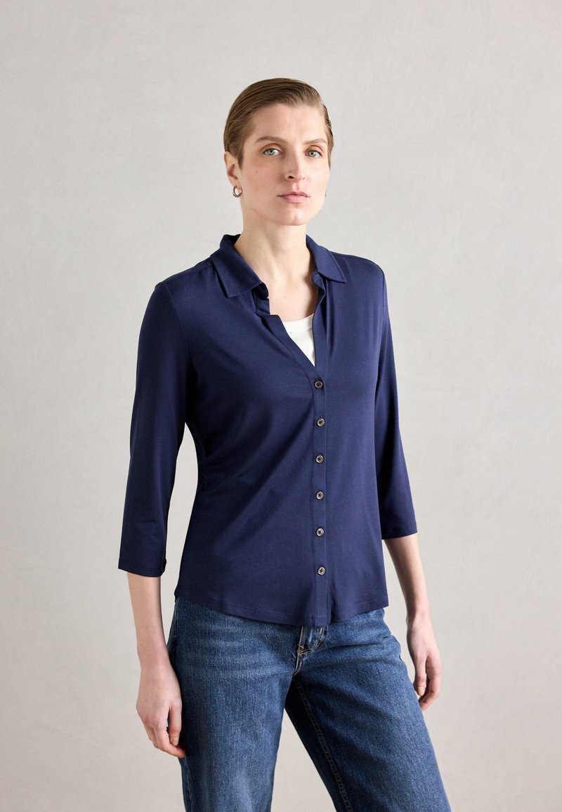 Marineblå skjorte med krage, trekvart ermer og avslappet passform, parret med blå denimjeans.