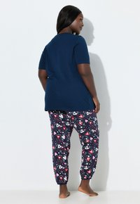 Laivastonsininen lyhythihainen t-paita yhdistettynä kuviollisiin pyjamahousuihin, joissa on punaisia ja vaaleanpunaisia sydämiä tummalla taustalla. Sileä puuvillainen materiaali.