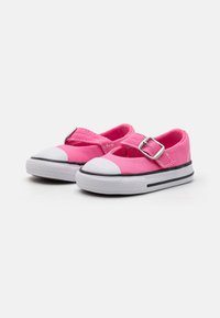 Zapatillas de lona rosas con punteras de goma blanca, rayas negras en la suela y una correa con hebilla plateada en la parte superior para un ajuste seguro.