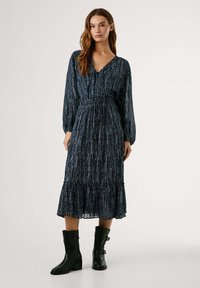 Abito lungo blu navy con strisce verticali argento, scollatura a V, maniche lunghe, vita cintrata e orlo arricciato. Abbinato a stivaletti neri fino alla caviglia.