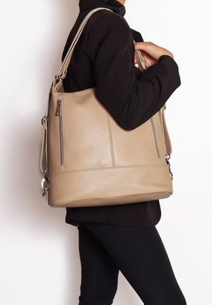Beige leren handtas met een gestructureerde afwerking, voorzien van twee zijritsen, een brede body en een lange verstelbare schouderband voor crossbody gebruik.