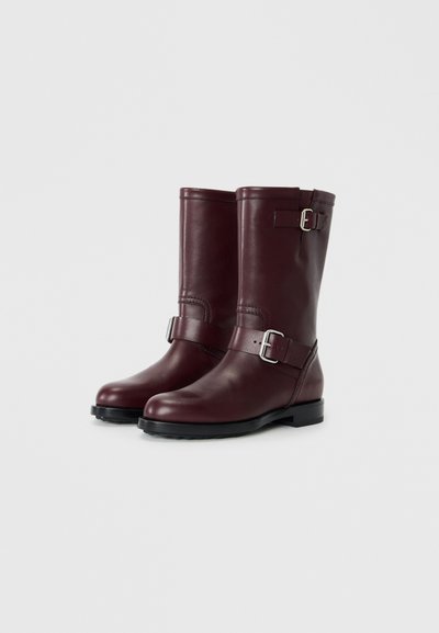 Marrón leather ankle boots with a round toe, side buckle accents, and a black rubber sole, featuring a smooth texture and sturdy design.