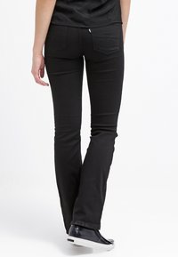 Jeans negros acampanados con una textura suave, bolsillos traseros y un detalle en la cinturilla. Combinados con una camiseta negra y zapatillas negras.