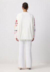 Üks suur valge t-särk, millel on värvilised lillemustrid varrukatel; sobitatud valgete laienevate pükstega ja igapäevaste jalanõudega.