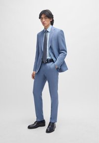 Fato azul claro com um blazer ajustado e calças ajustadas, combinado com uma camisa azul clara, uma gravata com padrão e sapatos pretos.