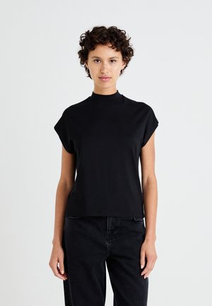 Haut noir à manches courtes avec col montant, en tissu lisse, coupe décontractée et design subtil au niveau des épaules, associé à un jean noir.