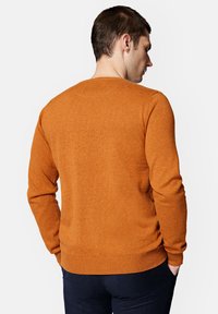 Pomarańczowy sweter z okrągłym dekoltem, z długimi rękawami, o dzianinowej strukturze i ściągaczu na dole. Widok z tyłu prezentuje gładkie wykończenie bez ozdób.