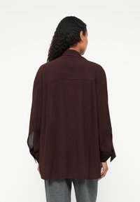 Burgundy košeľa na gombíky s voľným strihom, dlhými rukávmi a golierom. Obsahuje texturovanú látku a bočné rozparky pre pohodlný pohyb.