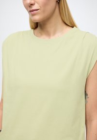 Haut vert clair à manches courtes avec un col rond et une texture douce. Présente des détails de couture subtils le long des épaules.