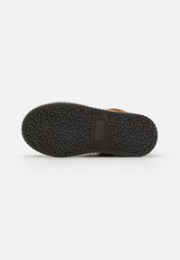 Semelle de chaussure en caoutchouc noir présentant un motif de bande de roulement géométrique, avec une section centrale légèrement surélevée et un bord lisse pour une meilleure adhérence.