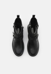 Botas negras hasta el tobillo con un upper de cuero suave, envoltura de tela negra texturizada, hebillas decorativas y un diseño de punta redonda.