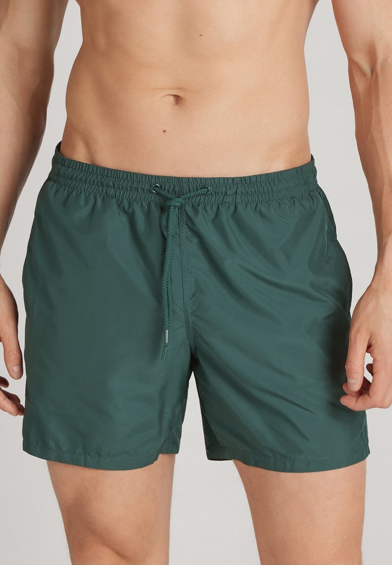 Zelené plavkové šortky vyrobené z lehkého, rychleschnoucího materiálu. Mají elastický pas s šňůrkou a hladký povrch. Bez kapes.