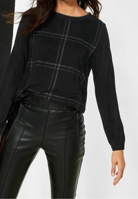 Svart långärmad topp med grå rutmönster, rund halsringning och texturerad tyg, i kombination med svarta läderbyxor med hög midja och dragkedjor.