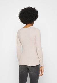 Světle béžový žebrovaný svetřík s dlouhým rukávem a kulatým výstřihem, přiléhavého střihu a hladké textury, nošený s tmavě šedými džínami.