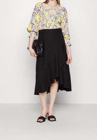 Haut jaune et lavande à motifs floraux et smocké ; jupe noire asymétrique avec ourlet volé ; pochette noire et sandales à talons.