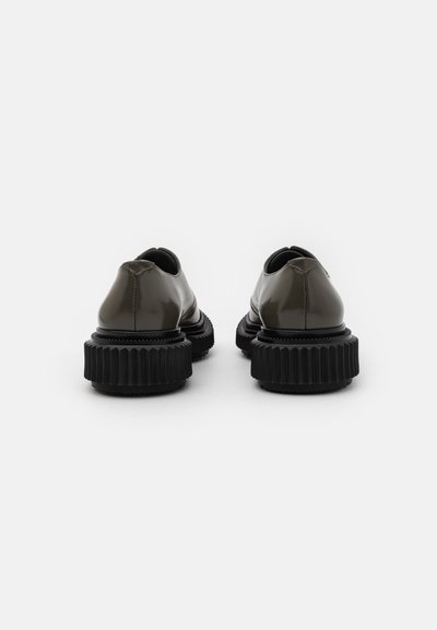 Dark green patent leather shoes with a thick black ridged sole. Rounded design and slip-on style without laces.