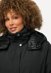 Chaqueta de plumas negra con cuello alto, cierre de cremallera y botones a presión. Presenta un tejido brillante en el cuello y un acabado texturizado.