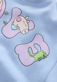 Hellblaues Sweatshirt mit Cartoonfiguren; zeigt ein Schwein und einen grünen Dinosaurier, umgeben von lila Formen und schwarzen Umrisslinien. Aus Baumwollmischung.