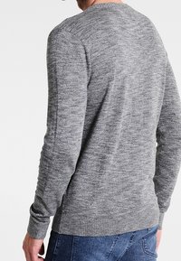 Šedý pletený svetr s kulatým výstřihem, zdobený texturovaným vzorem a žebrovanými manžetami a lemem. Nosit s modrými džíny.