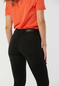 Jean noir taille haute en denim, avec un design classique à cinq poches, des passants de ceinture et une étiquette en cuir sur la taille.