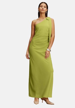 Woman wearing a floor-length, one-shoulder lime green dress with high-heeled sheer shoes and silver hoop earrings and bracelet.