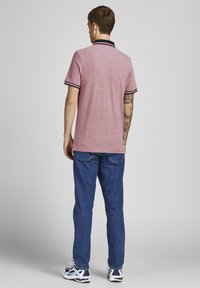 Rød heather polo skjorte med en sort krave, der har røde og hvide striber. Sammen med blå jeans og sportssko.