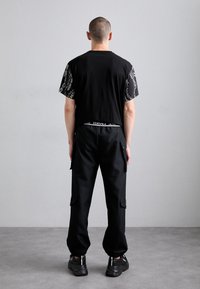 T-shirt preta de manga curta com mangas estampadas, combinada com calças cargo pretas com bolsos laterais e punhos elásticos.