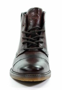 Brązowy skórzany botek za kostkę z zaokrąglonym noskiem, sznurowanym zapięciem, szczegółami stębnowania i teksturowaną podeszwą. Posiada wytłoczone logo na języku.