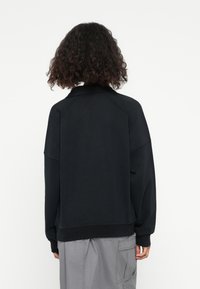 Černá oversized mikina se vsazenými rukávy, ribbed manžetami a lemem. Jemná látka, minimalistický design, žádné viditelné loga nebo vzory.