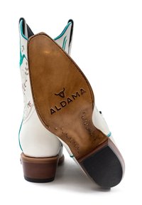 Stivale da cowboy bianco con accenti turchesi, dotato di ricami floreali, un tacco in legno e una suola in pelle marrone contrassegnata "ALDAMA".