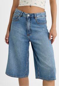 Pantalones culottes de mezclilla azul claro con cintura alta, que incluyen bolsillos y costuras a contraste. La tela tiene una textura ligeramente descolorida.