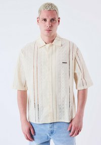 Korte mouwen, crèmekleurig shirt met een patroonstructuur, voorzien van knoopsluiting en dunne strepen. Gemaakt van lichtgewicht stof.