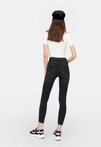 Jeans skinny negros de talle alto, con bolsillos traseros destacados, combinados con una camiseta blanca de manga corta y sandalias blancas chunky.