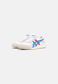White sneakers with blue and red accents, a textured mesh upper, flat white laces, and a cream rubber sole, featuring a low-top design.