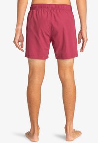 Shorts de baie roșii cu talie elastică, fabricate dintr-un material ușor, au un design simplu și se așază puțin deasupra genunchiului.