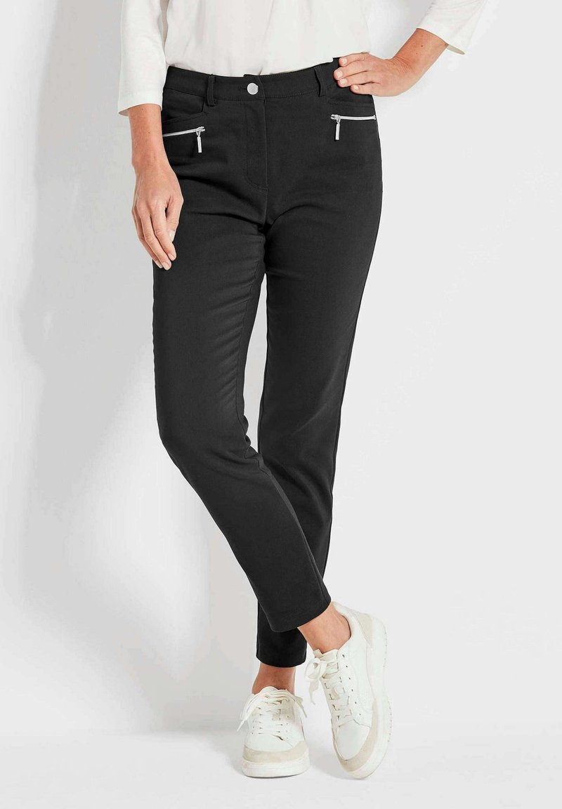 Pantalons noirs à coupe slim, dotés de deux poches zippées et d'une texture lisse. Portés avec des baskets blanches pour un look décontracté.
