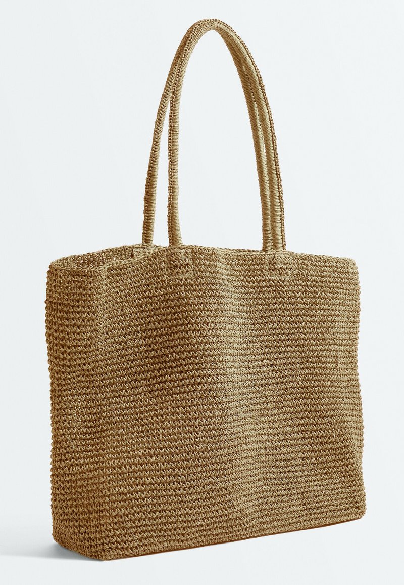 Sac cabas en paille tressée marron avec deux longues anses et une forme rectangulaire sur fond blanc.
