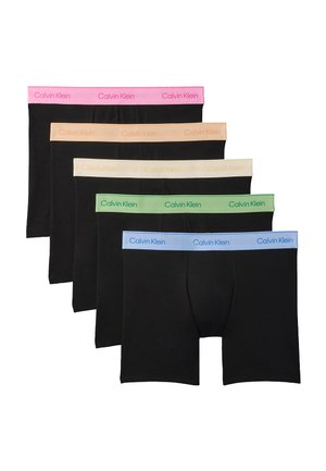 Oberkörperfreier Mann steht barfuß, trägt schwarze Boxershorts mit einem pinkfarbenen Calvin Klein Bund und richtet den Bund mit beiden Händen.