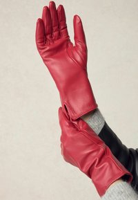 Czerwone skórzane rękawiczki o eleganckim wzornictwie, dopasowanych palcach i otwartym mankiecie. Gładka tekstura bez widocznych elementów metalowych czy wzorów.